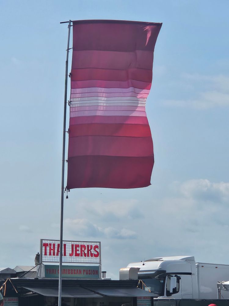 A large festival flag with 15 horizontal stripes, in various shades, of red, pink and white.