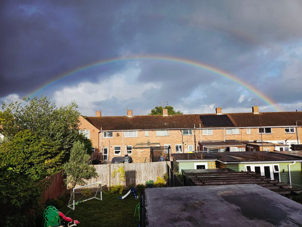 A clear double rainbow over a row of brown brick buildings. The sky is dark and its about to rain again!