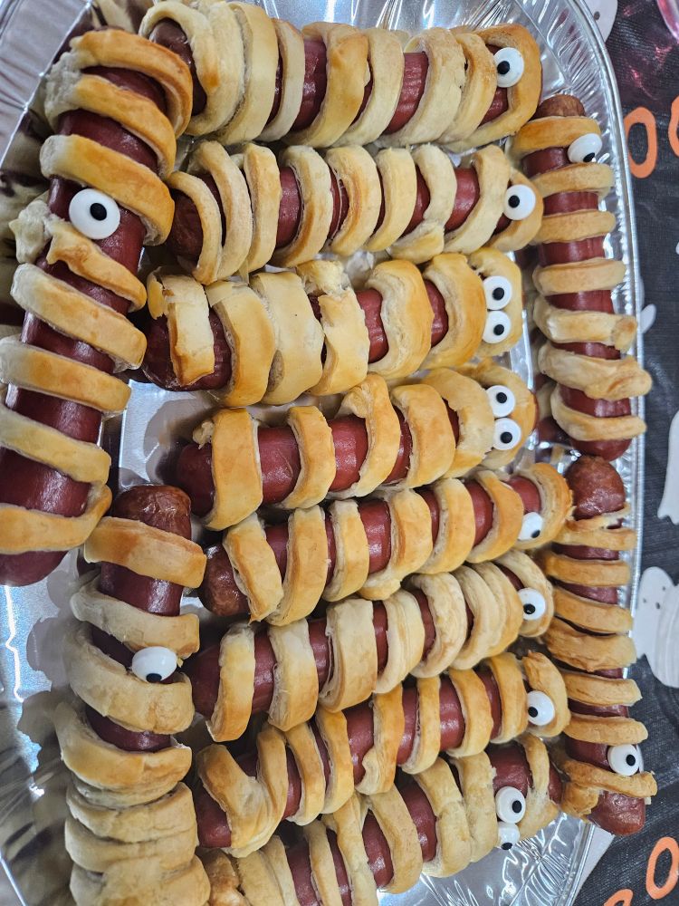A silver foil plate filled with sausages wrapped in pastry mummy-style, they have edible google eyes on them.