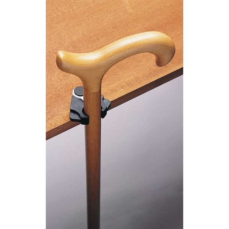 [A light wood walking sticking is held up by a black metal device against a wood table]