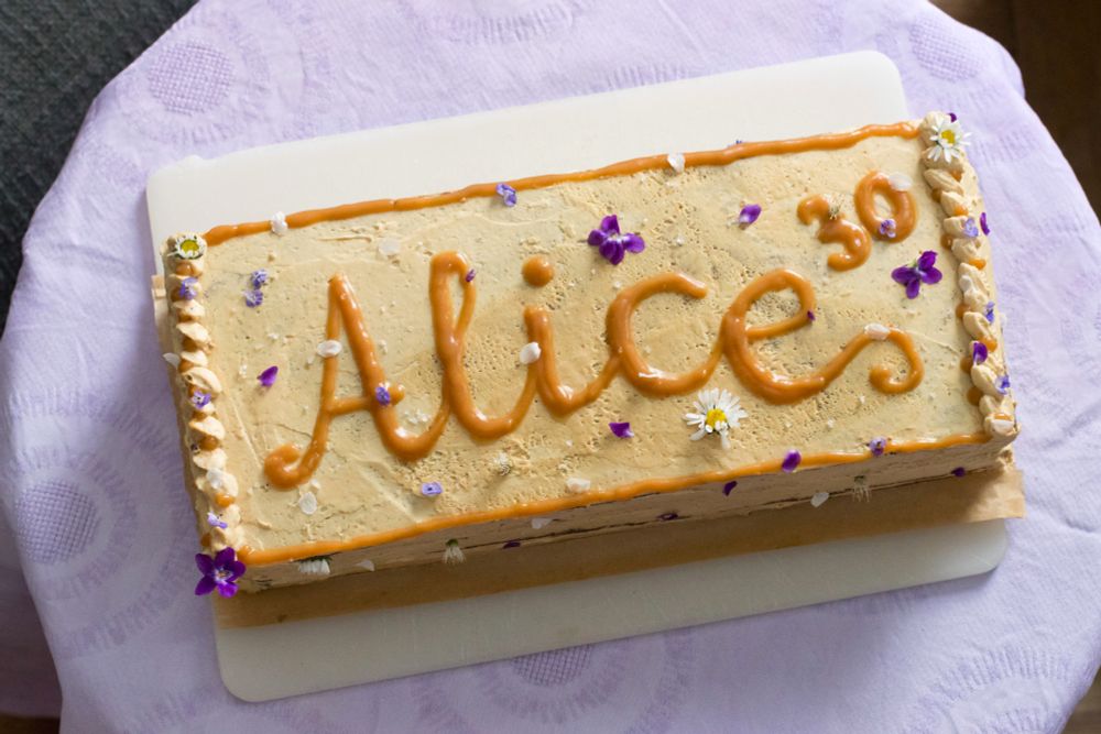 eine karamellfarbene rechteckige Torte mit der Aufschrift "Alice 30" und vielen Blüten