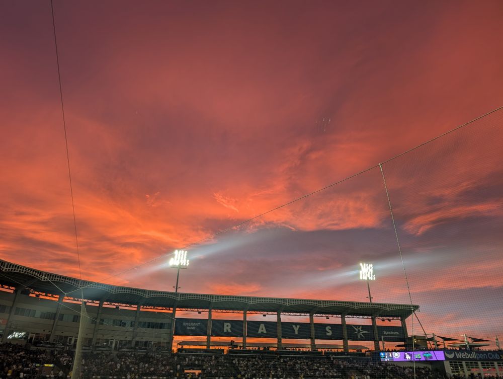 Clouds glowing orange in the sunset, viewed from inside a baseball stadium