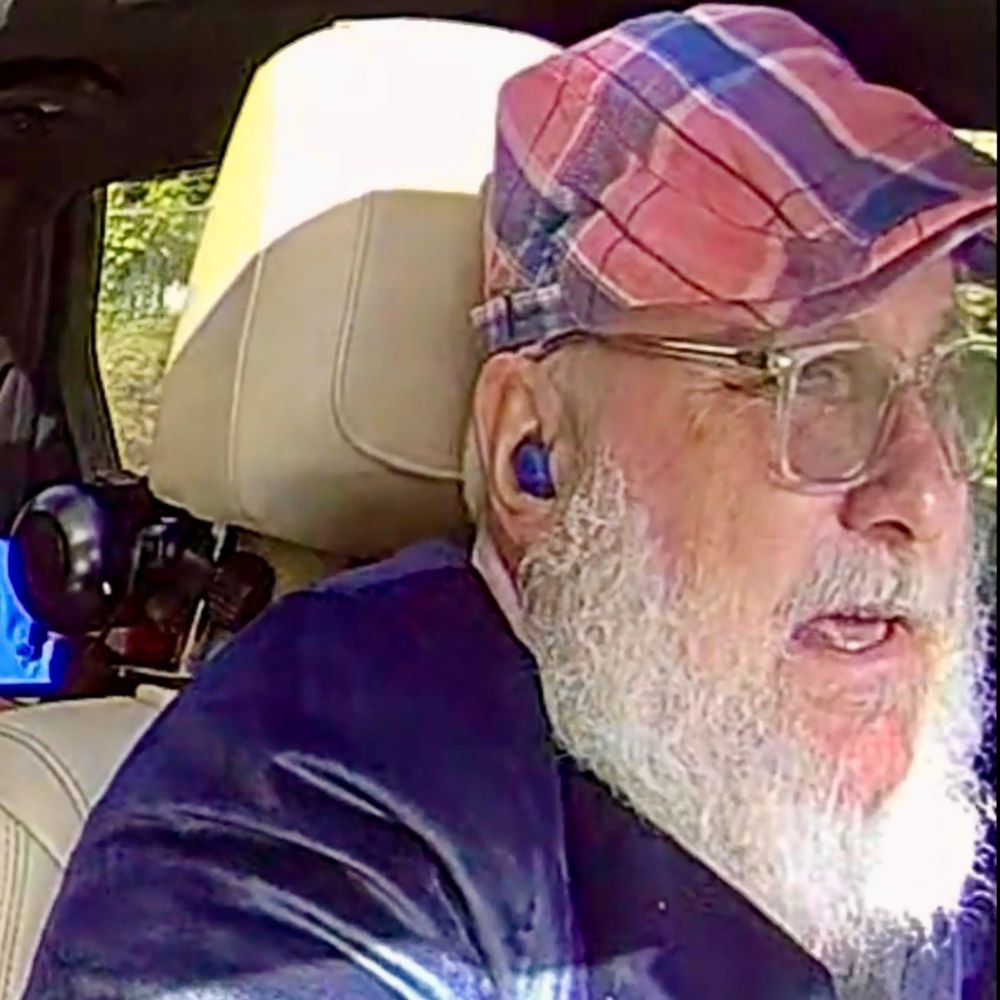 old guy in a blue & pink suit tells a story while driving