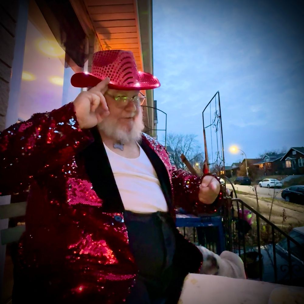 old guy in a red glitter cowboy hat and tuxedo jacket saluting on his front porch