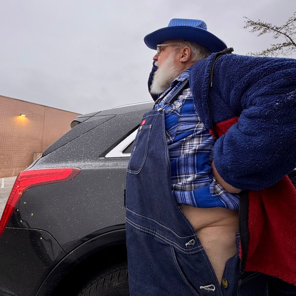 old guy in blue denim deals with the side buttons of his overalls being unbuttoned and his loose-fitting underwear falling down around his knees 