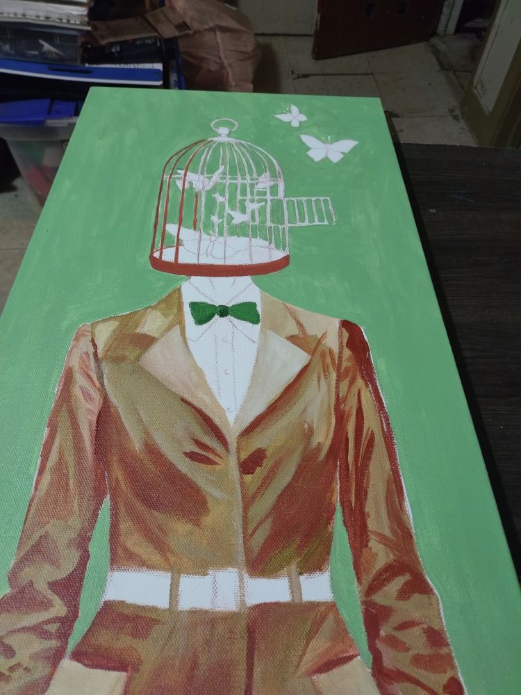 A full-length view of a painting-in-progress on a long, narrow canvas with a bright mint-green background. A figure wearing a tailored brown jacket, white shirt, and a deep green bow tie stands centered. The head is replaced entirely by an open birdcage. Butterflies are depicted escaping the cage, with two butterflies flying freely above it. The figure’s face is missing, suggesting a focus on constraint and liberation.