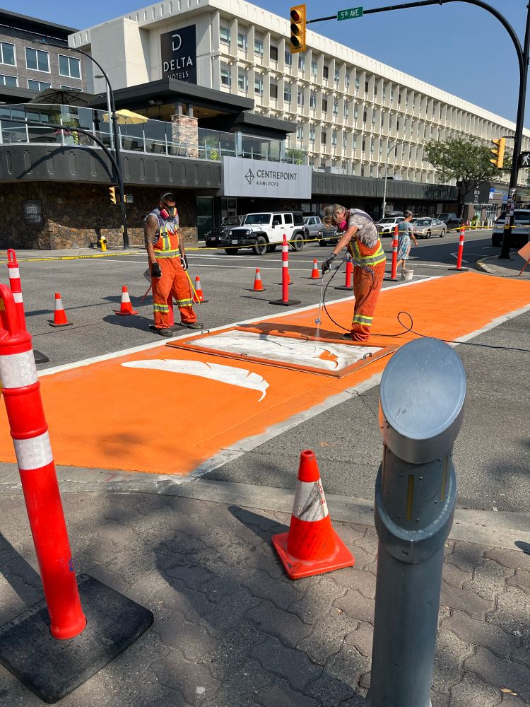 Two workers paint orange crosswalk in Kamloops 