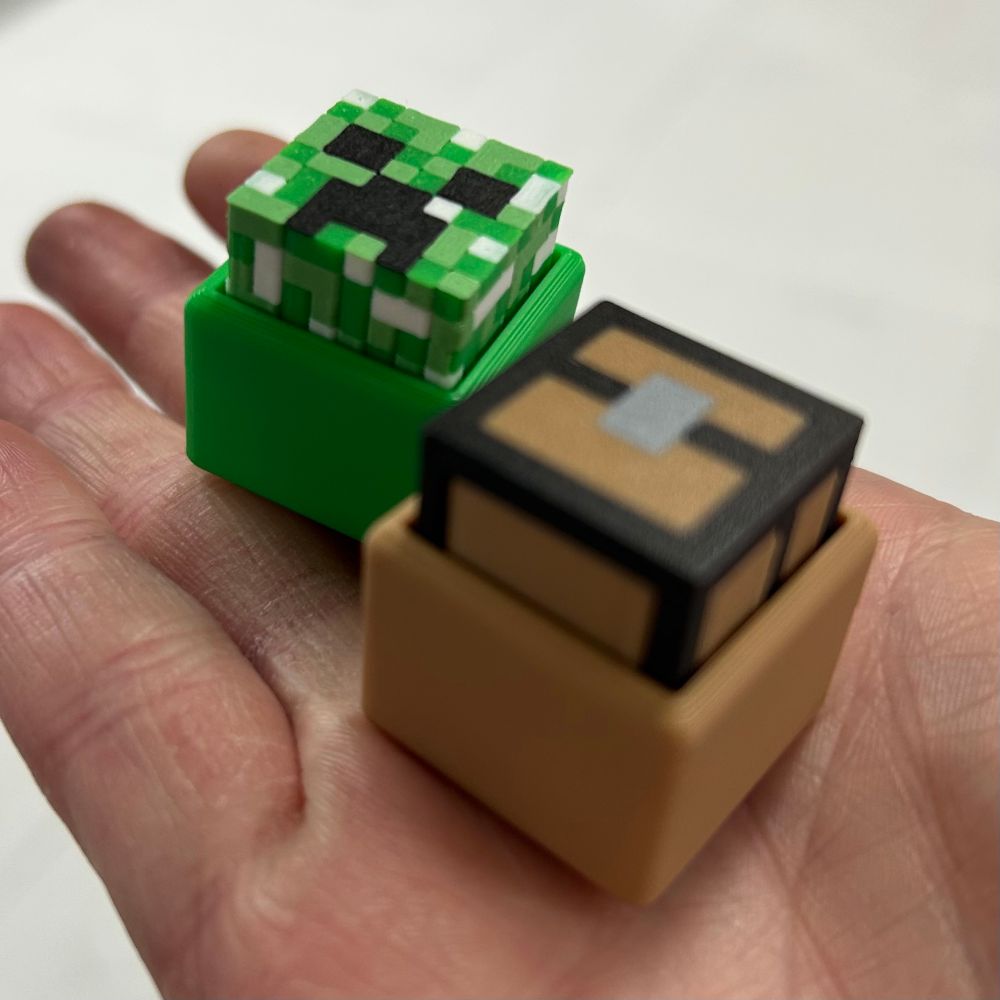 Two small cubes. One is painted green like a creeper and the other is painted brown and black like a treasure chest. 