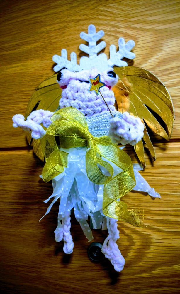 A knitted frog in a sparkly fairy/angel outfit attached to a front door. 