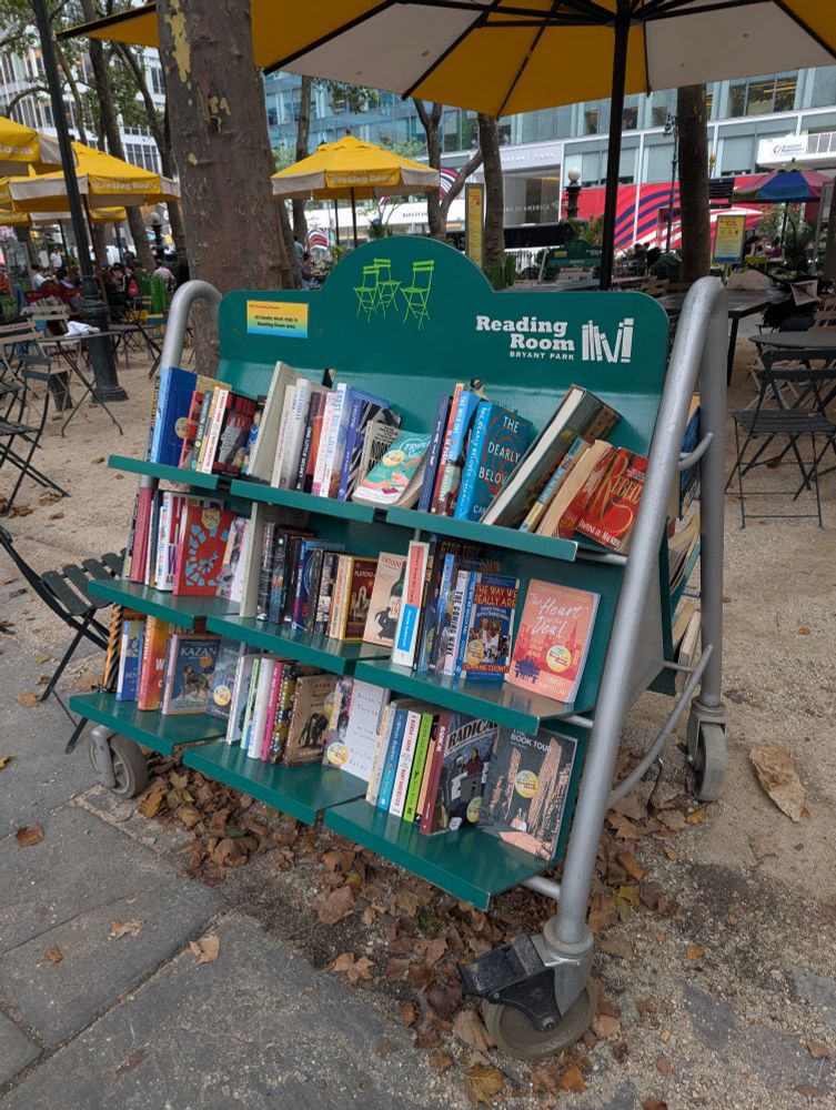 Bryant Park NY reading room mobile book stand features books of all levels available without check out for people to read nearby in the park. 