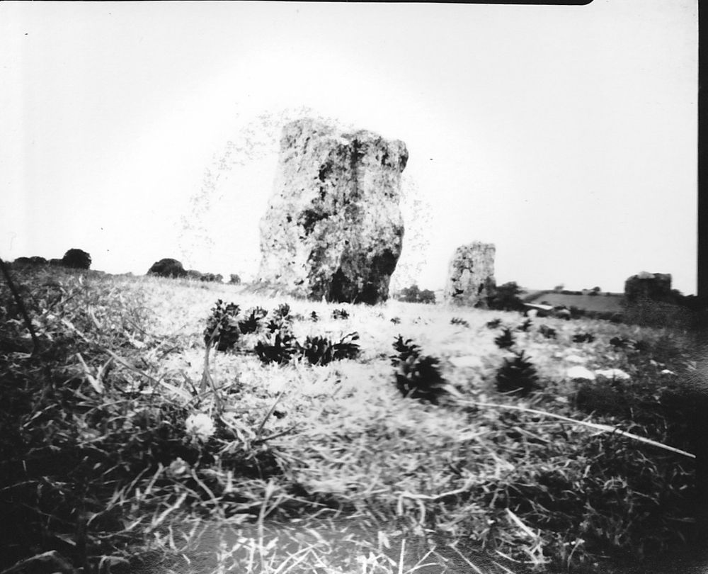 Black and white pinhole photograph across the grass showing standing stone