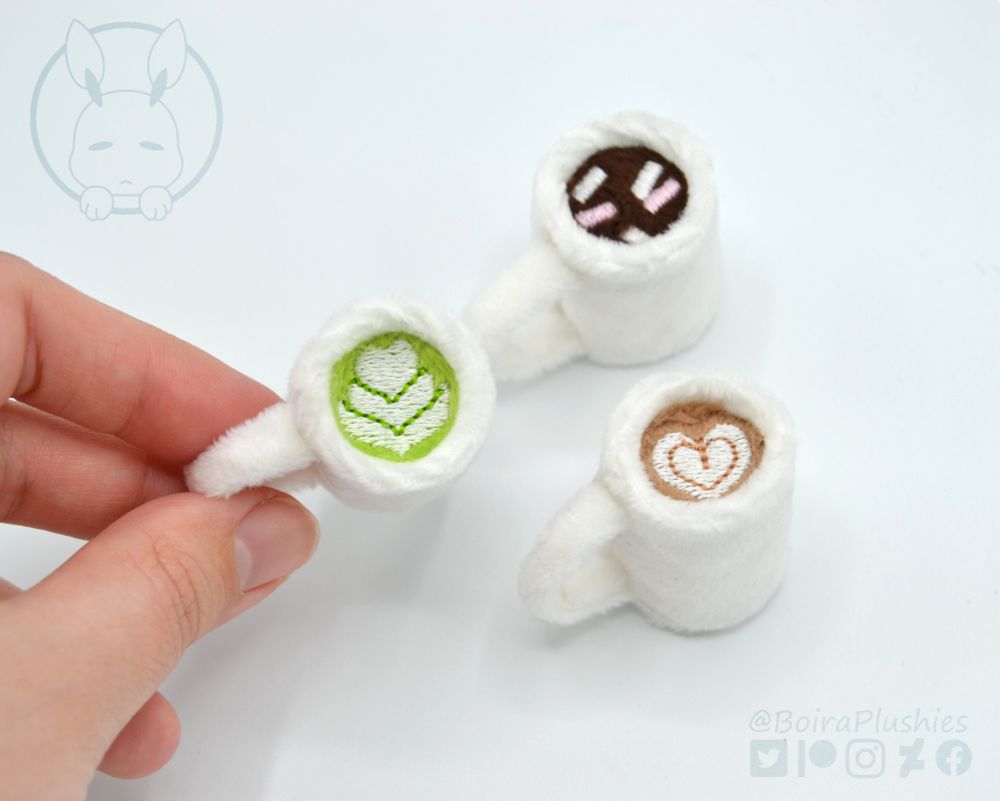 Three small plush mugs, each one with a different beverage: matcha latte, hot cocoa with marshmallows and coffee latte