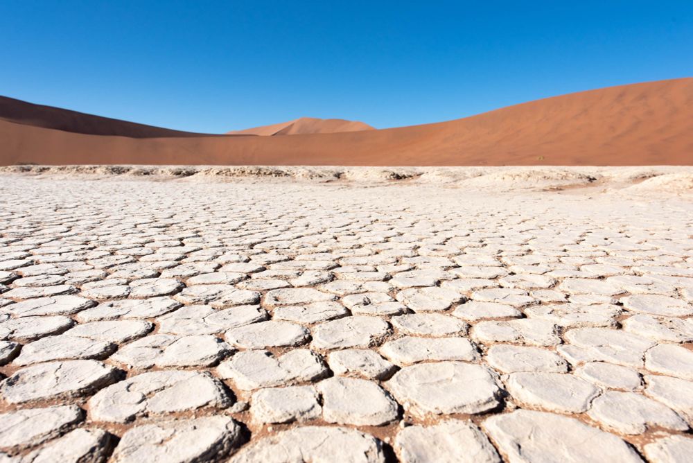 Image of the dry clay pan at Deadvlei, Namibia.  Hexagonal shapes surrounded by massive sand dunes and immense blue sky 