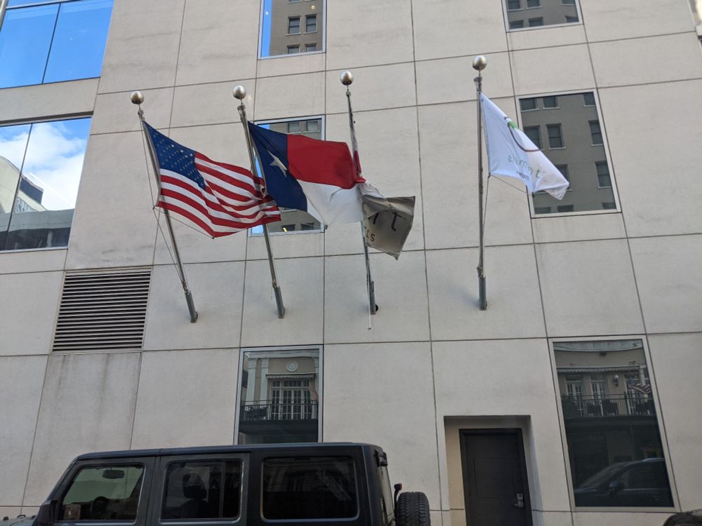 A building facade with several flags flying, one of which is an upside-down Texas flags.
