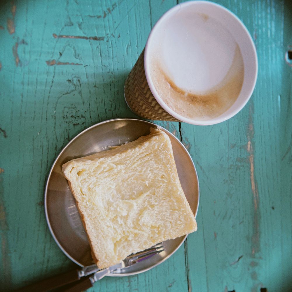 A cup of cappuccino and a piece of fluffy pastry on a metal plate.