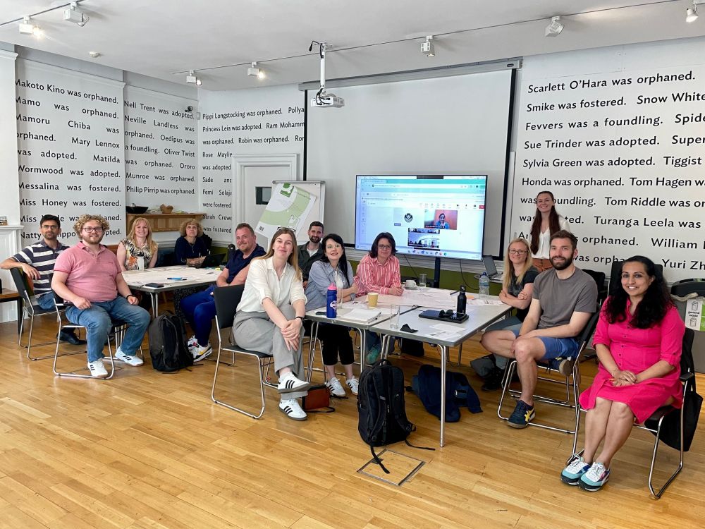 Staff all pose for the camera surrounding tables filled with board paper, pens and note pads.