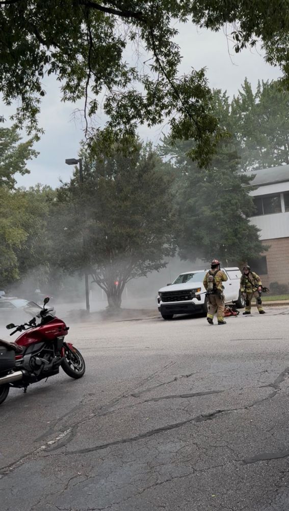 Two firemen in front of a building with white smoke coming from the side of it.