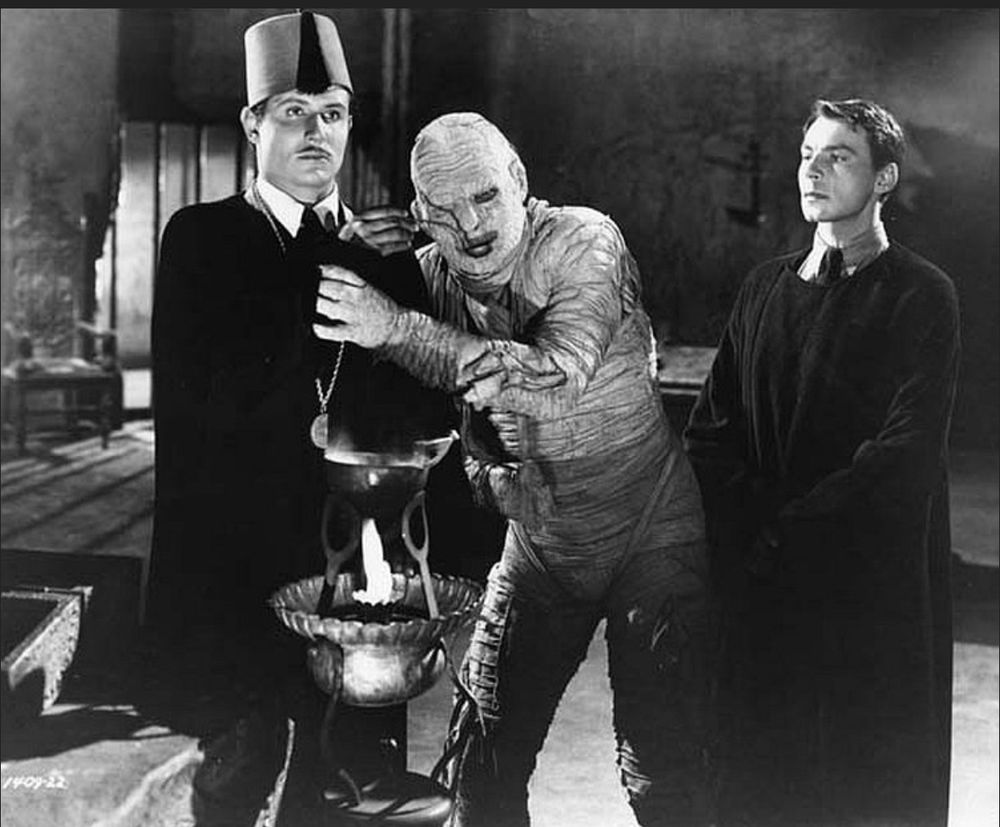 Two men give tana leaves to a living mummy in a crypt
