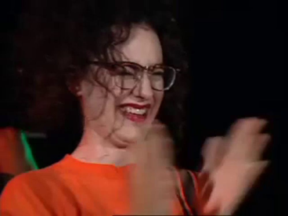 a woman wearing glasses and an orange shirt is laughing in a dark room .