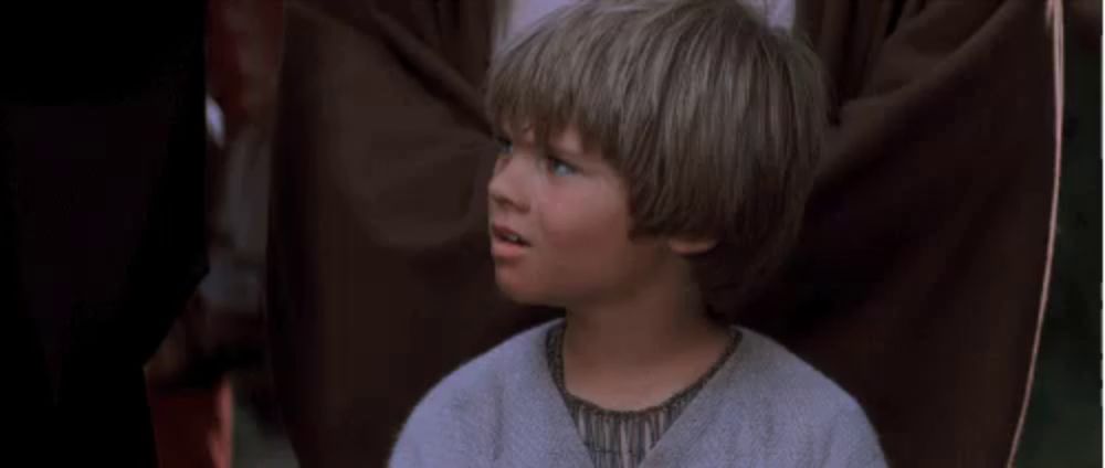 a young boy with blonde hair and blue eyes is sitting in a chair .