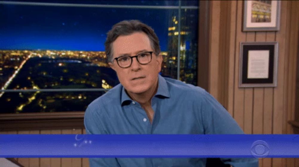 a man wearing glasses and a blue shirt stands in front of a screen that says cbs on it