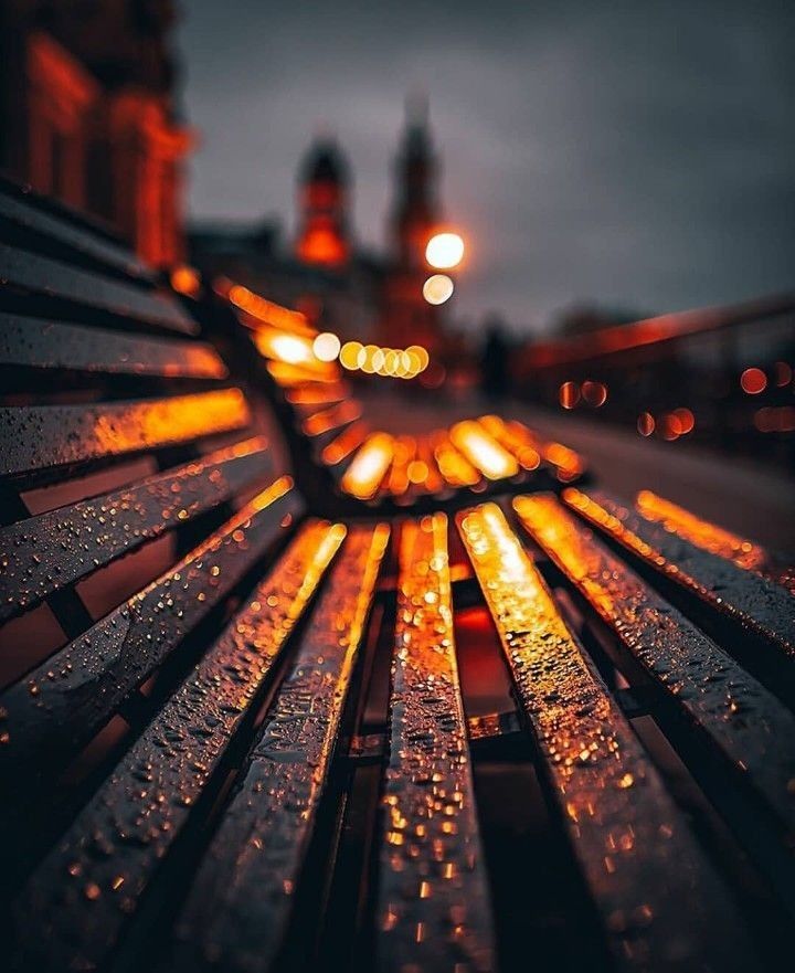 Banc trempé de pluie, les lumières de la ville sont floutées en arrière plan.
