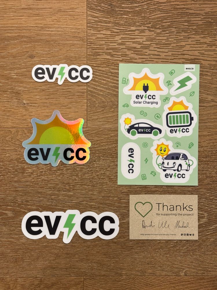 Drei Sticker und ein Stickerbogen mit EVCC-Motiven sowie eine Dankeschön-Karte auf einem Holzboden.