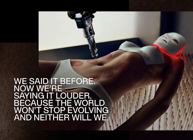 A very skinny lady in white underwear, including a molded plastic chest plate with hard nipples, laying on a bed of long sharp nails with a robot injection arm above her stomach that's covered in red cupping marks. She's wearing a white mask that's glowing red light underneath it on to her face. The text "WE SAID IT BEFORE.
NOW WE'RE
SAYING IT LOUDER.
BECAUSE THE WORLD WON'T STOP EVOLVING AND NEITHER WILL WE."