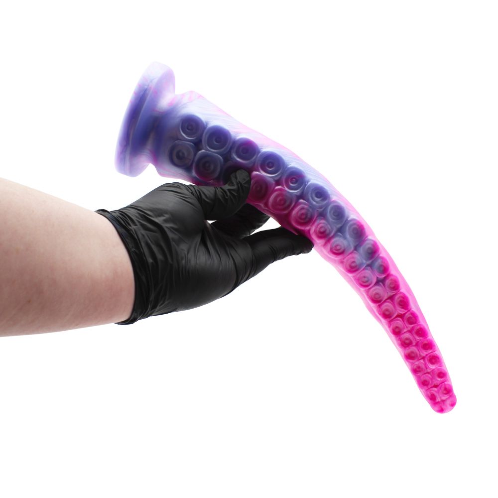 A white person's gloved hand holding a foot-long tentacle dildo. The tentacle is draped over, showing off 2 rows of circular suckers adorning the front side.