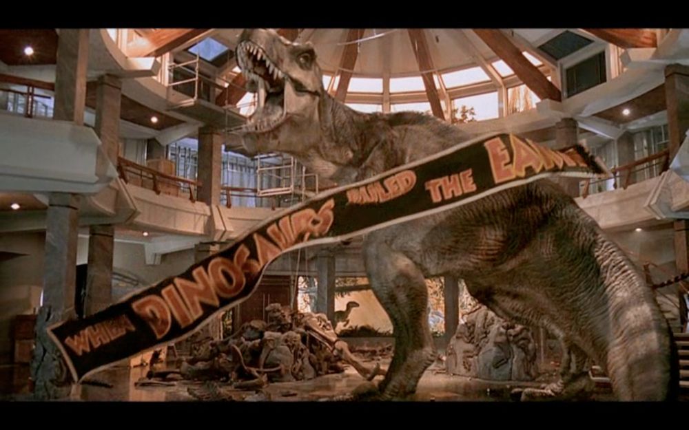 “When dinosaurs ruled the world” banner with a Tyrannosaurus rex tearing it down from Jurassic Park movie