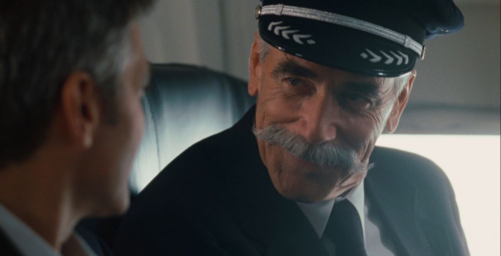 Mustachioed pilot congratulating a passenger for excessive flying