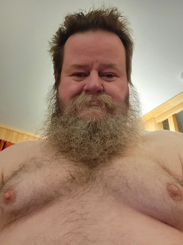 Bearded shirtless man with a hairy chest regards the camera.