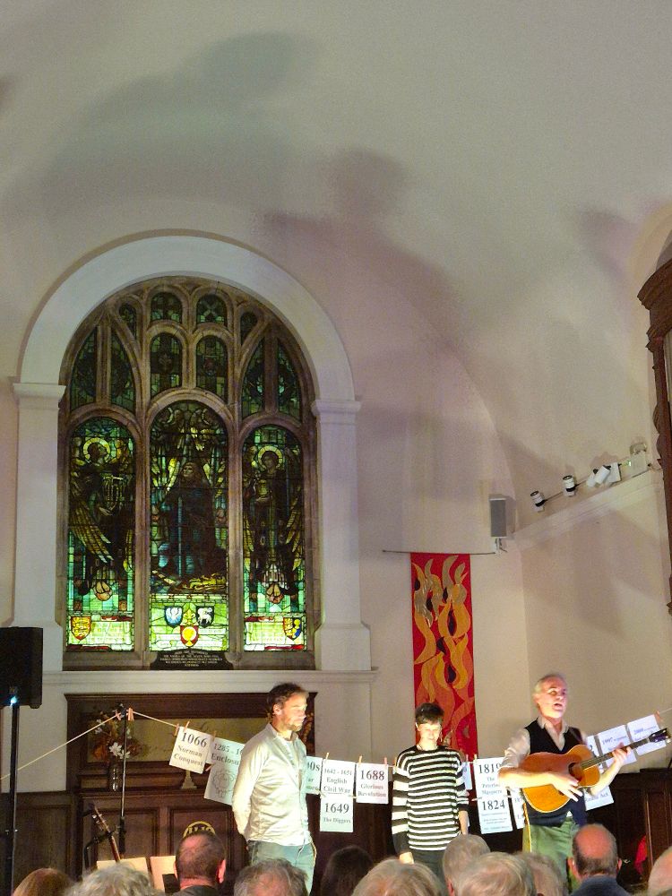 The cast of 'Three Acres And A Cow' starting the final song in the show, with the completed 'Washing Line of History' and the beautiful arched stained glass window of the Wesley Church, Chester behind. them