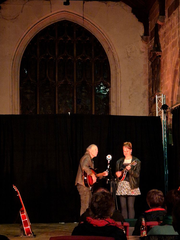 Brooks Williams with guitar and Vera Van Heeringen with mandolin, both playing and singing into an ambient mic on stage in St Mary's Creative Space (the former church of St Mary on the Hill, Chester)