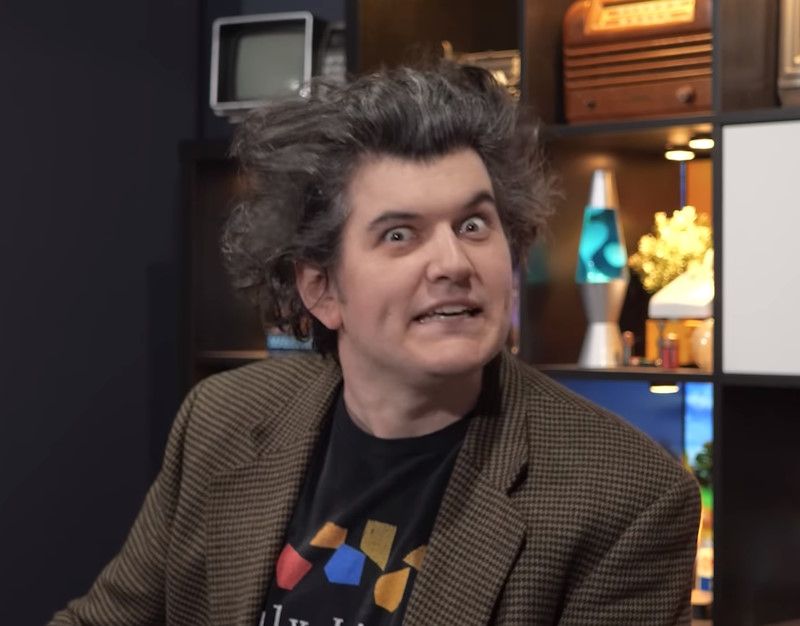 A screenshot from the Technology Connection video, showing Alec Watson looking into the camera with a wild expression on his face and his hair made to stand up from his head to give him a crazy look.