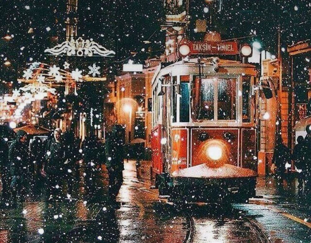 Rotes Weihnachtstram bei Schneegestöber. Auf der Seite wartende Personen. Im Hintergrund Weihnachtsbeleuchtung