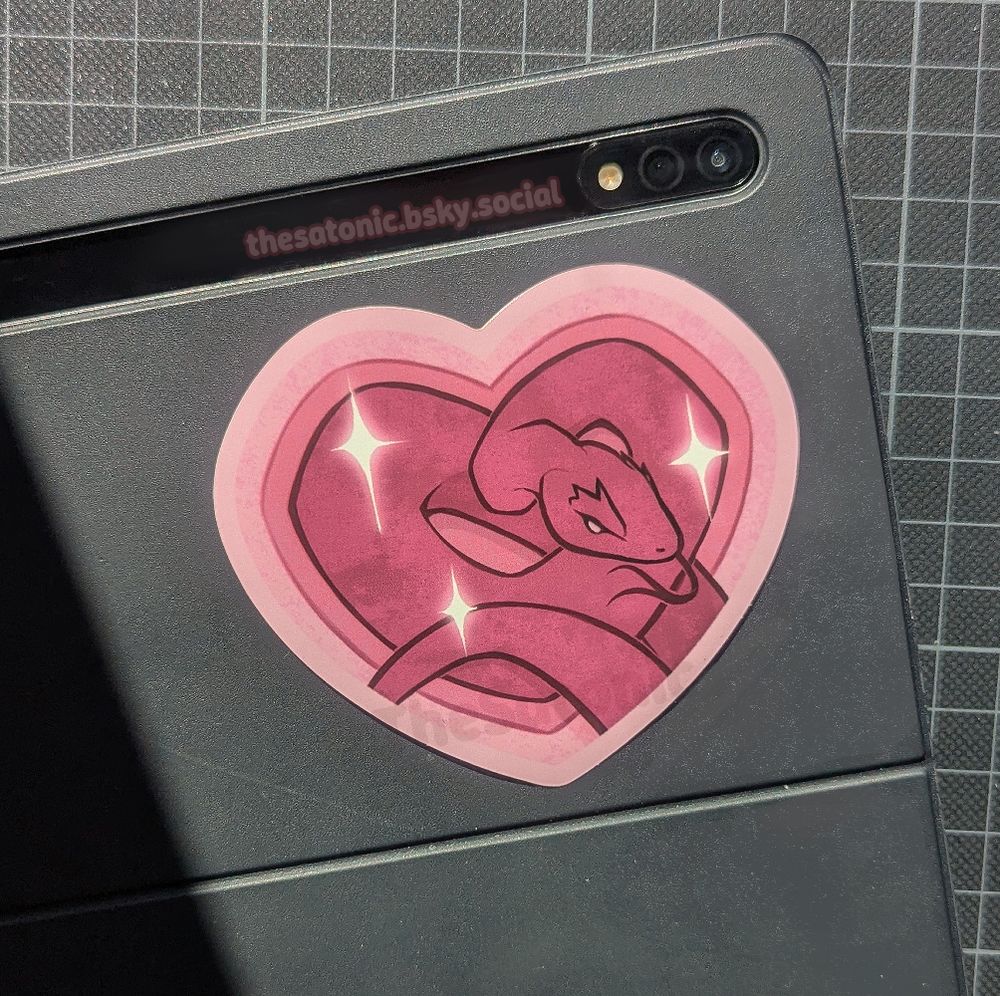 A pink, heart-shaped die cut sticker showing a pink snake, curled up.