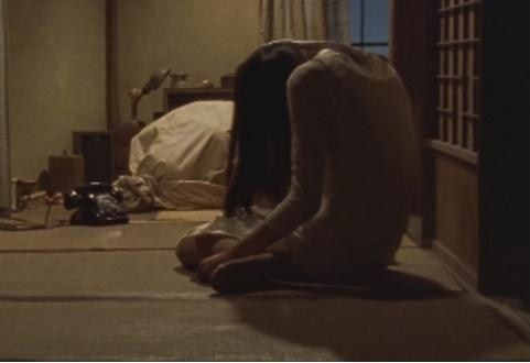 A woman is crouched on the floor in a dark room next to an old fashioned dial phone and a bag

This is the scene from Audition where the phone rings and she answers and you find out what is next to her is the still alive mutilated body of one of her husbands in a large canvas sack