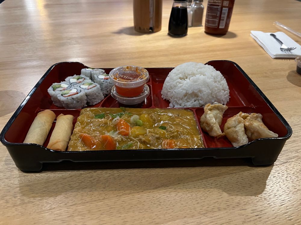 A set dinner of chicken curry, fried gyoza, spring rolls, rice, sushi, and sauce. 