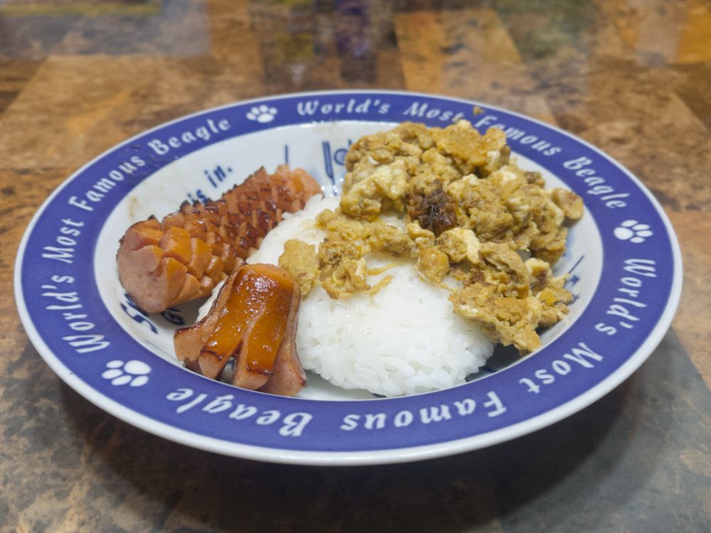 Bowl of a sausage (majority cut cross hatched and crispy, but there’s also an octopus shaped one) and scrambled eggs over rice. The eggs are a bit off color. 