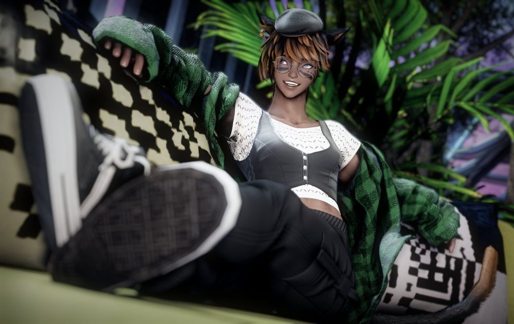 Catte, in comfortable clothes and loose flannel jacket off-shoulders. She is lounging with legs up and crossed on a Solution 9 cafe sofa, and arms resting up on the back and pillows.