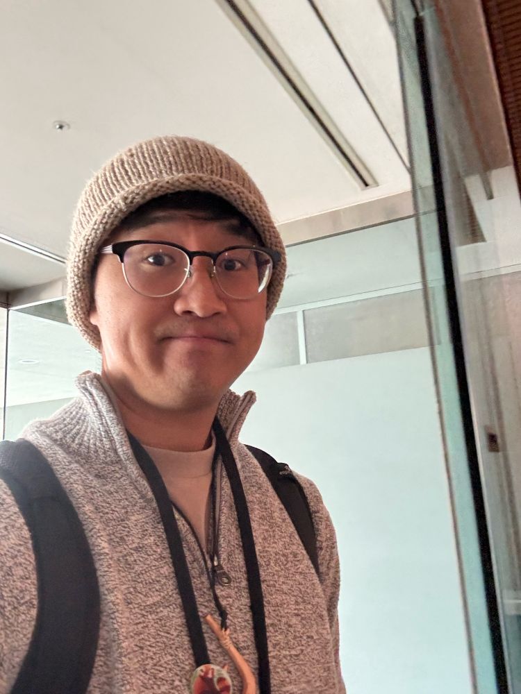 Asian male trying to stay warm at FC2024. Wearing a hei matau and badge made by Spalding.