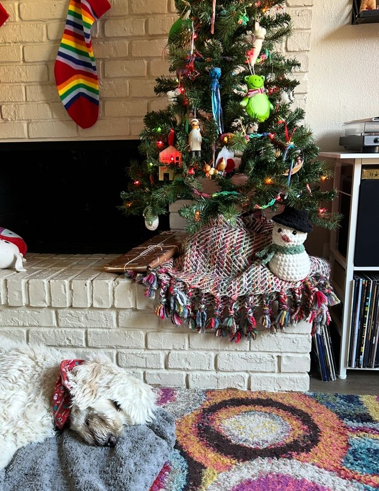 a big white fluffy dog sleeping under a little christmas tree