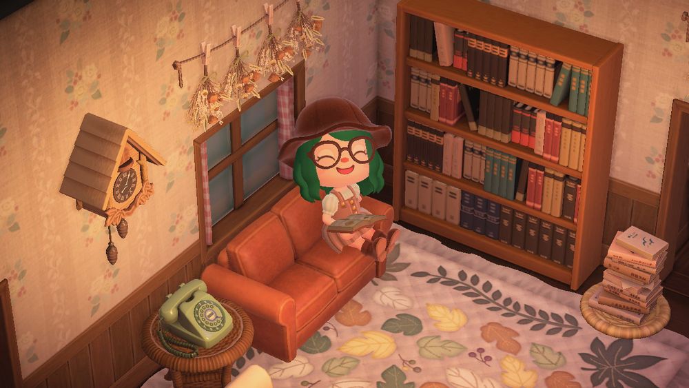 lohla’s animal crossing character sits on the couch in their living room with a book