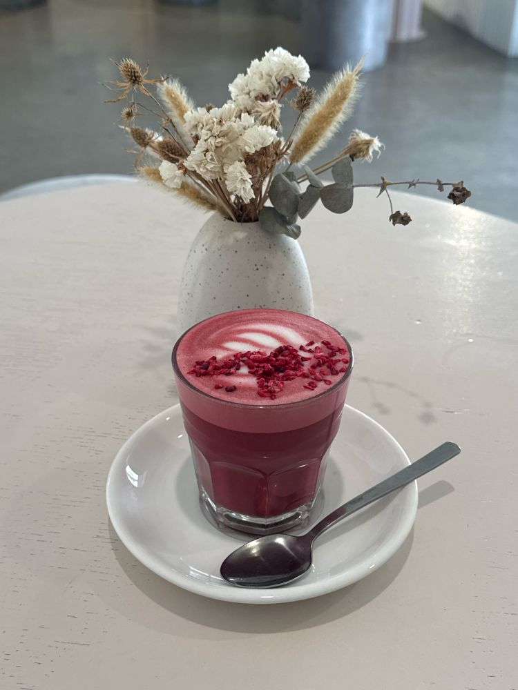A “red velvet latte” on a plate with a spoon on a table with some flowers
