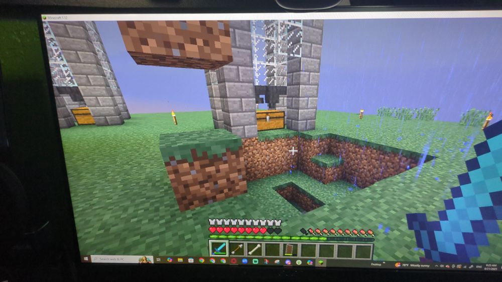 A photograph of a computer monitor displaying the voxel game "Minecraft." There is a giant hole in the ground.