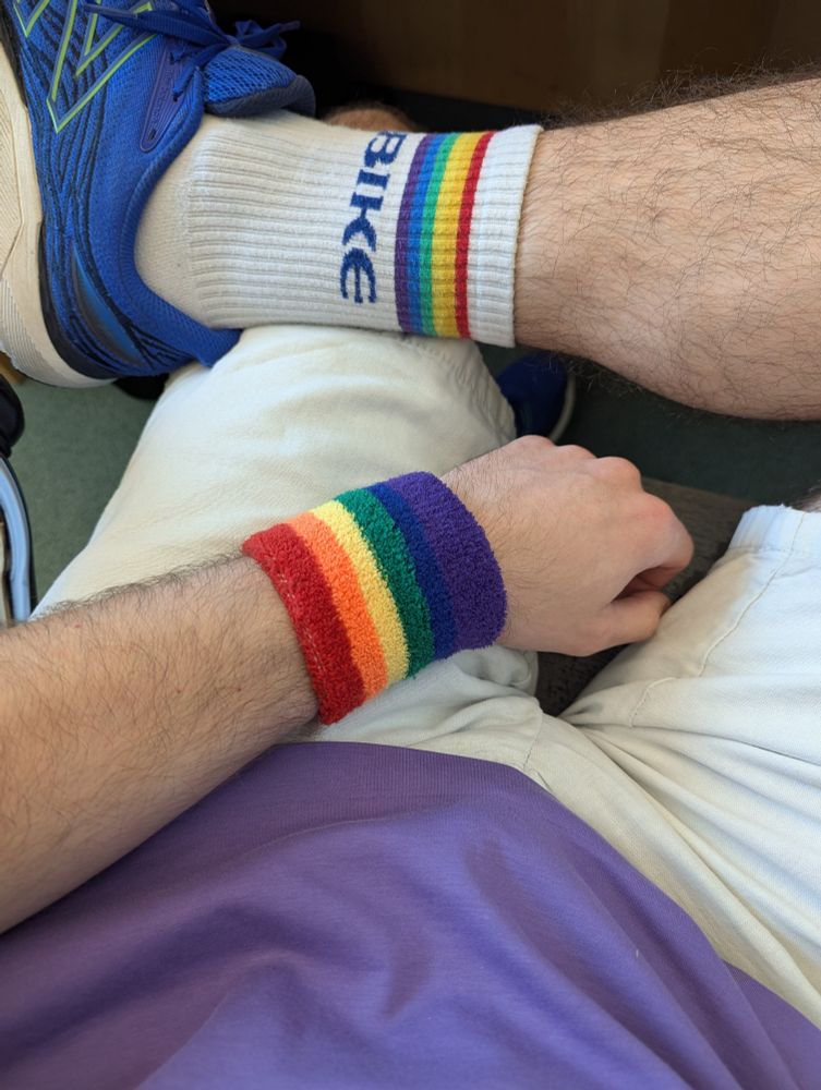 Delta wearing a purple shirt, rainbow armband, and pride socks