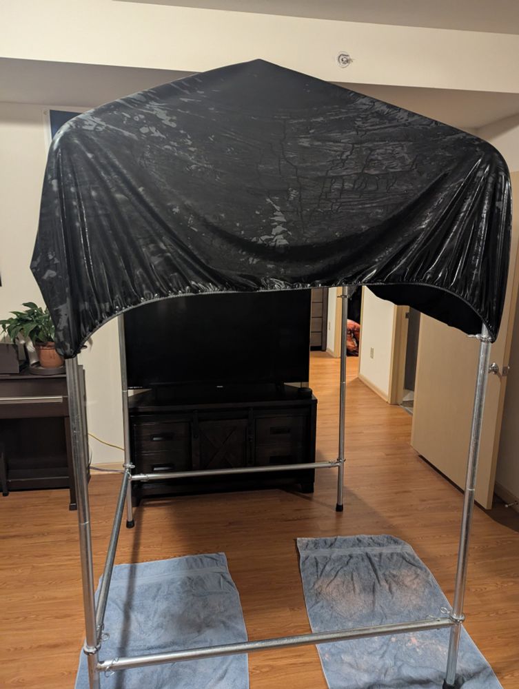 black fluidproof play sheets, draped to dry over a metal sling, in a living room