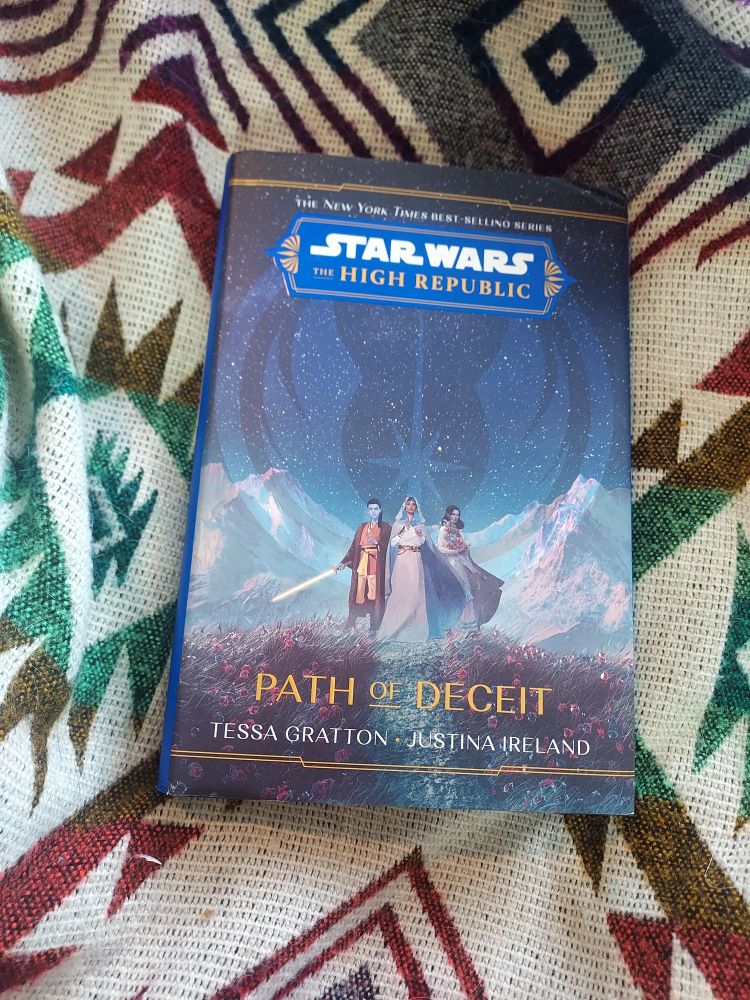 Cover of Star Wars: The High Republic, Path of Deceit by Tessa Gratton and Justina Ireland. Depicts three robed figures, one with a lightsaber, in a field of pink flowers under a starry sky. The jedi logo is faintly superimposed over the scene.