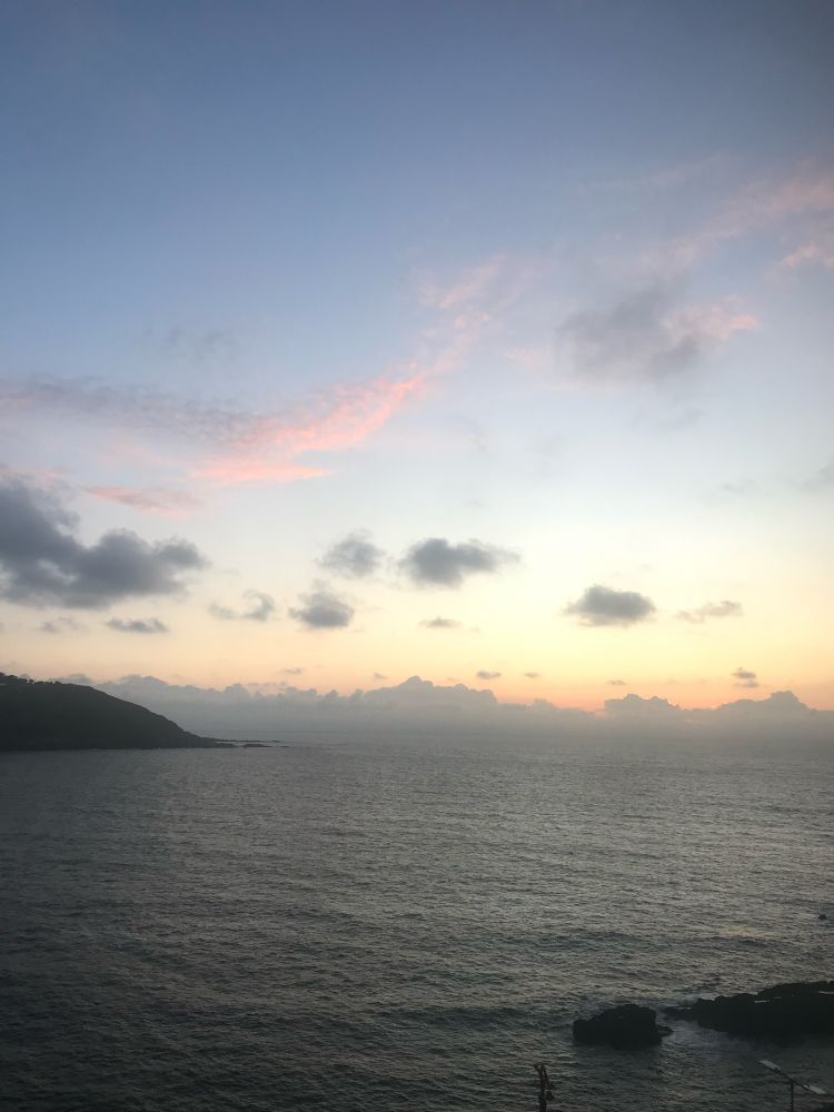 Puesta de sol, viéndose el mar y un horizonte anaranjado con una pocas nubes